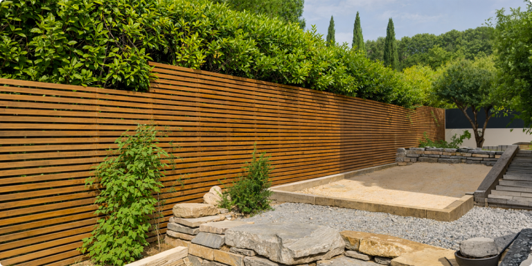Clôture bois claire-voie moderne en lames horizontales dans un jardin paysager avec massif minéral et haie dense