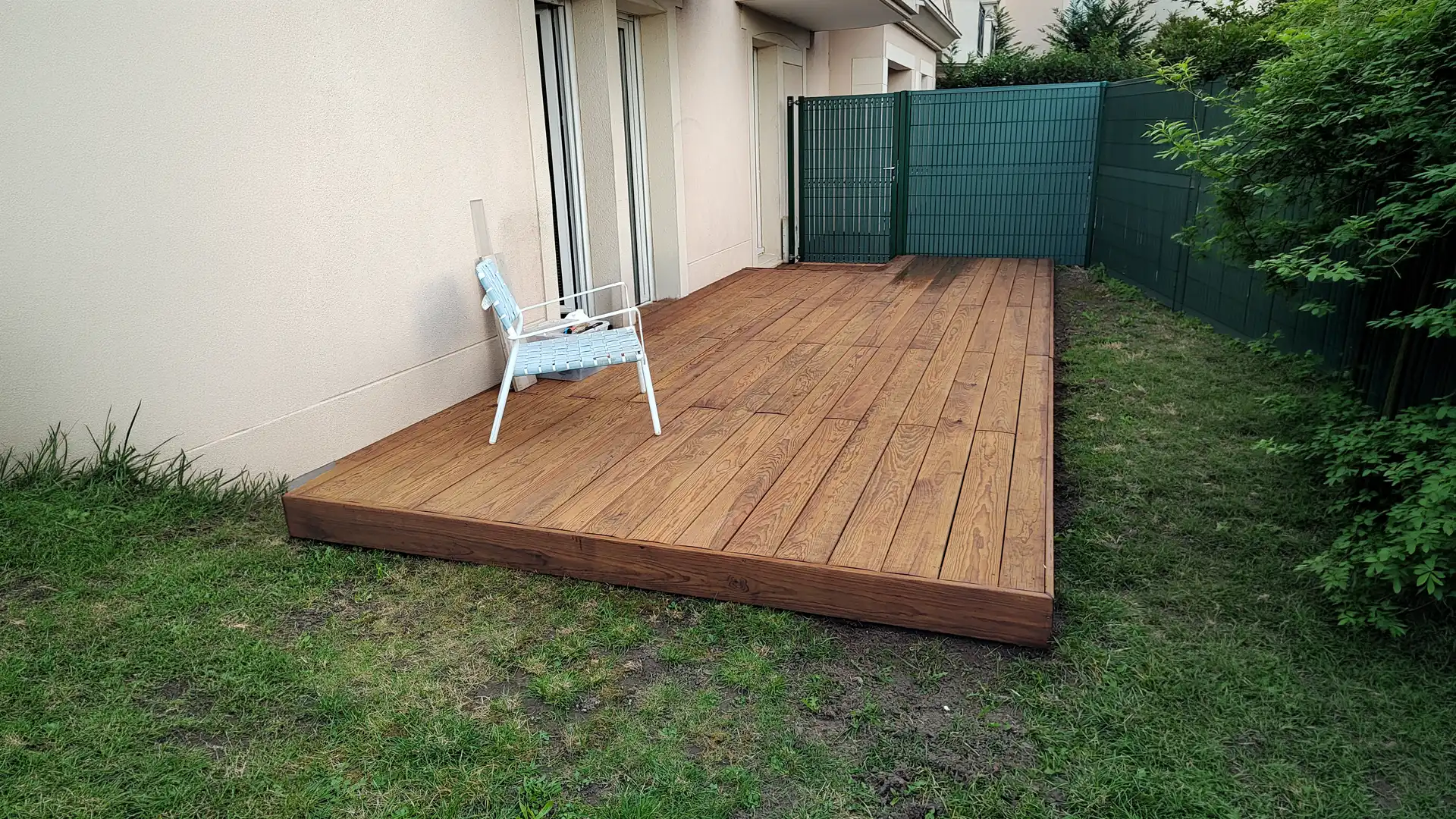 terrasse en bois rectangulaire installée dans un jardin avec clôture et chaise extérieure