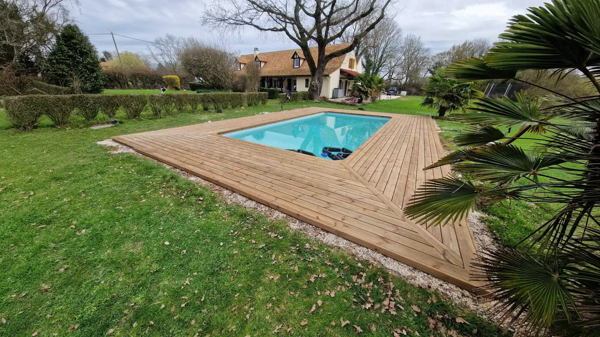 grande terrasse en bois autour piscine rectangulaire dans un jardin avec maison et espace vert