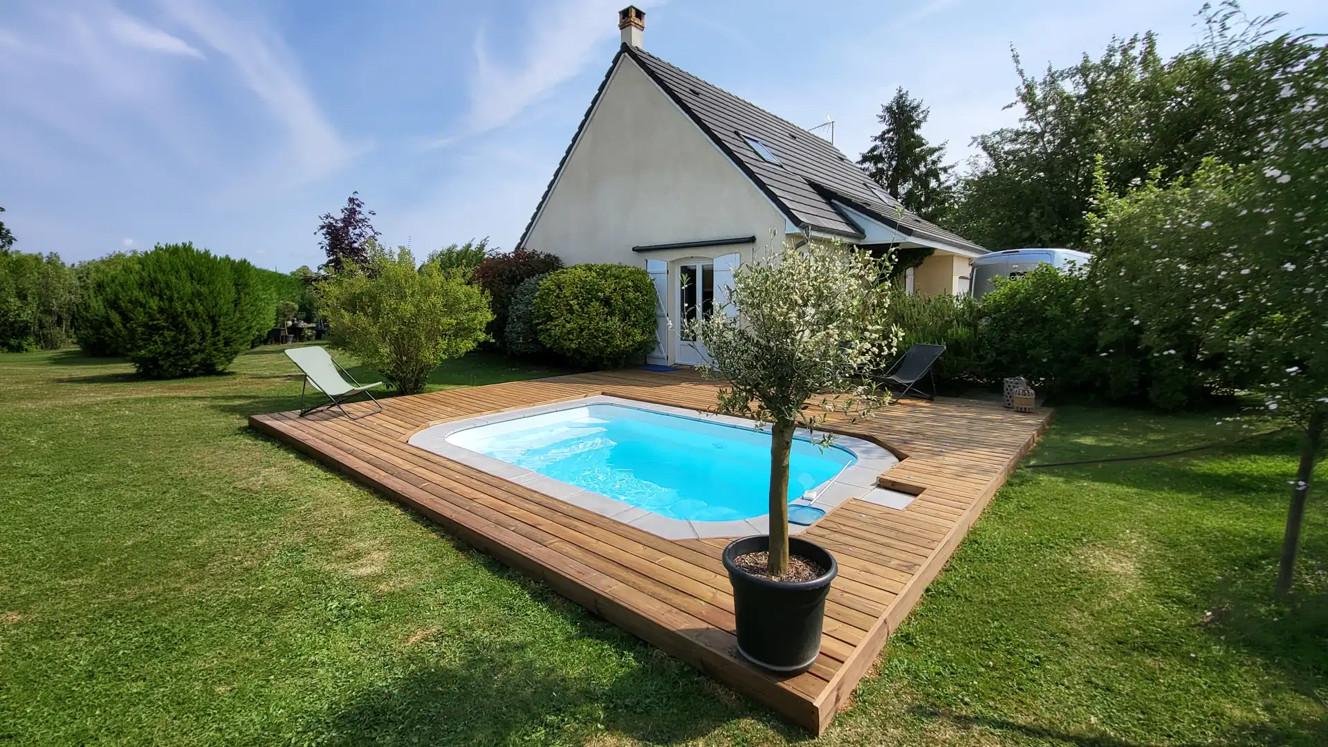 terrasse en bois avec piscine devant maison individuelle et jardin arboré avec transats