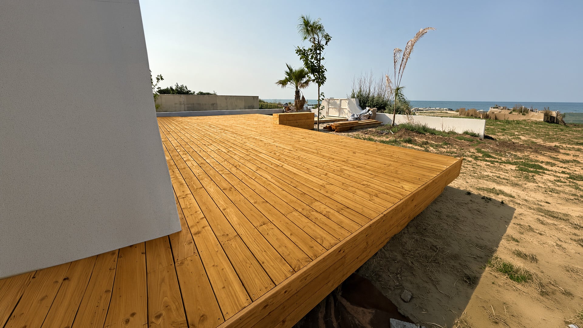 Grande terrasse en bois et façade en bardage bois entretenues et protégées, aménagées avec mobilier de jardin et plantes décoratives.