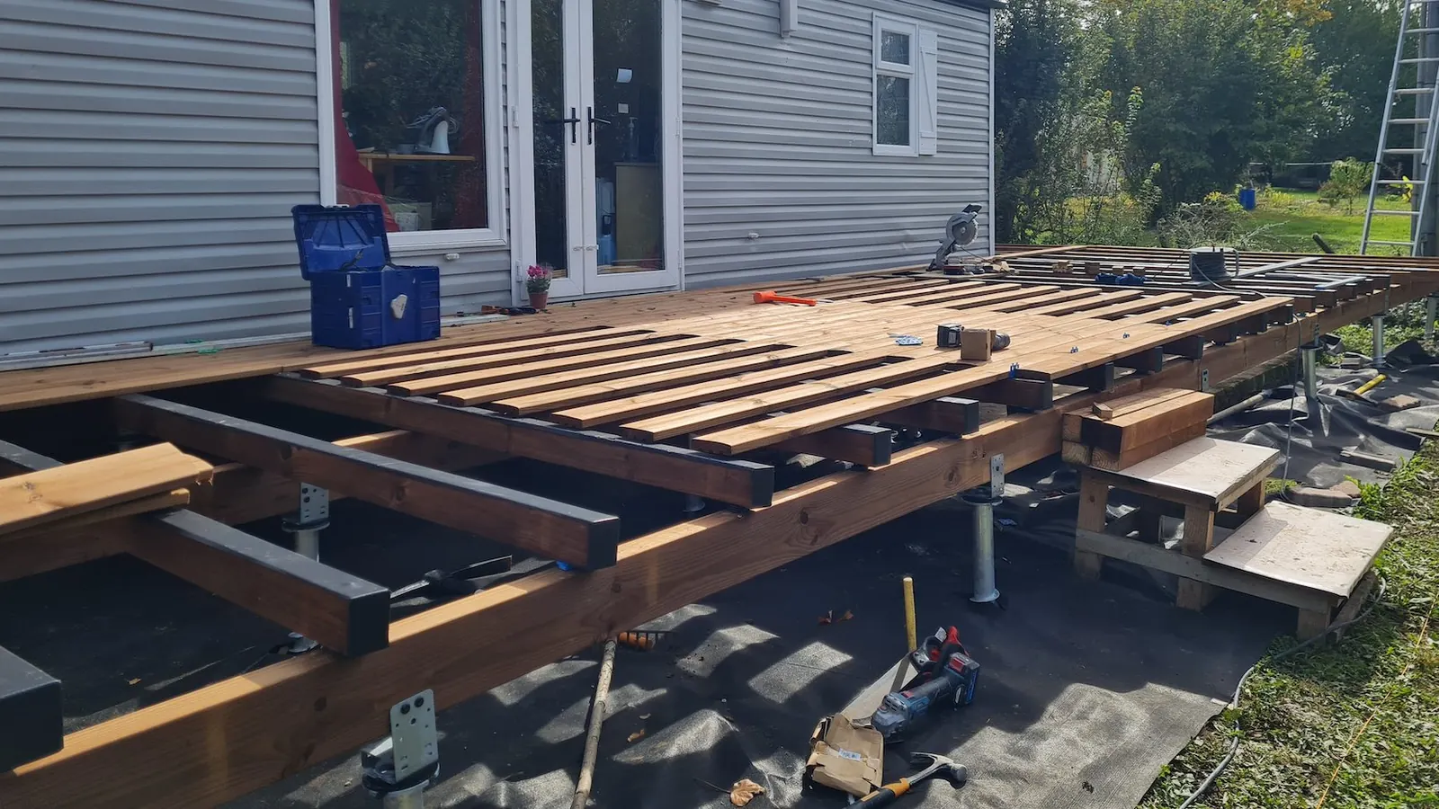 Terrasse bois sur pilotis : guide complet (structure, pose, prix au m²) 3 Structure d'une terrasse bois sur pilotis en cours de pose : solives pin classe 4 sur vis de fondation acier galvanisé vissées dans le sol