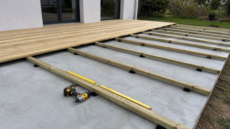 Chantier de pose d'une terrasse bois pin autoclave classe 4 sur dalle beton avec lambourdes fixees sur cales plastique noires, visseuse et niveau a bulle