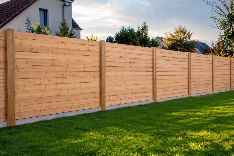 Cloture en bois Douglas clair a lames horizontales posee dans un jardin, poteaux reguliers sur plots beton, pelouse au premier plan