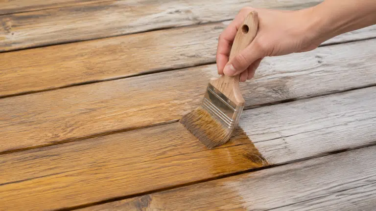 Application d un saturateur teinte miel au pinceau sur les lames grises d une terrasse en bois